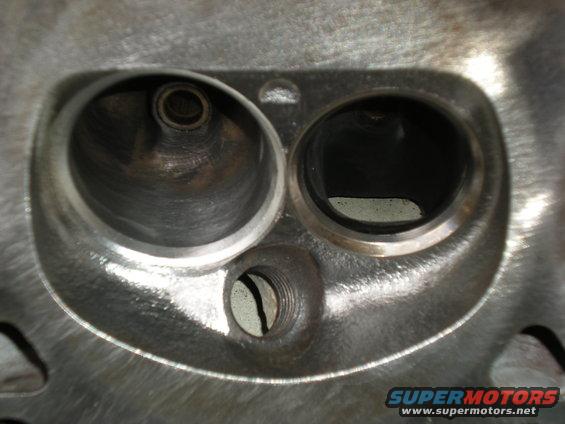 Close-up of an engine cylinder head with two large valve openings and a smaller threaded hole