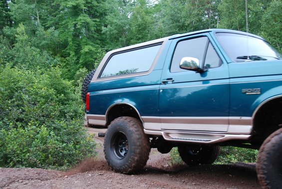 Teal Ford Bronco on dirt road, spare tire on back. Looks like a 1996 model
