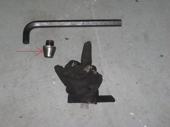 Hex wrench and a lug nut on a concrete floor. Red arrow points to the lug nut