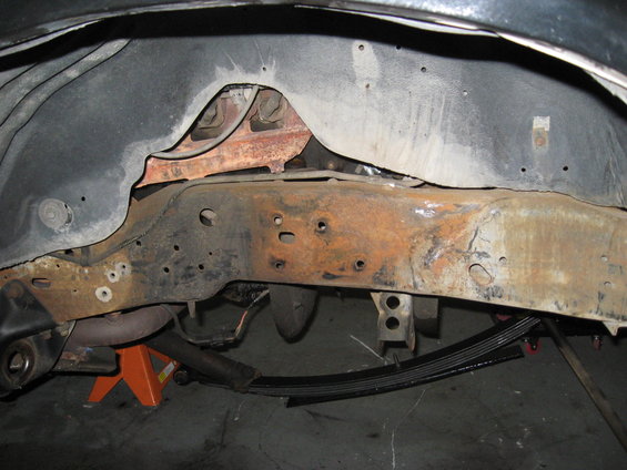 close-up of rusty vehicle frame and leaf springs, supported by an orange jack