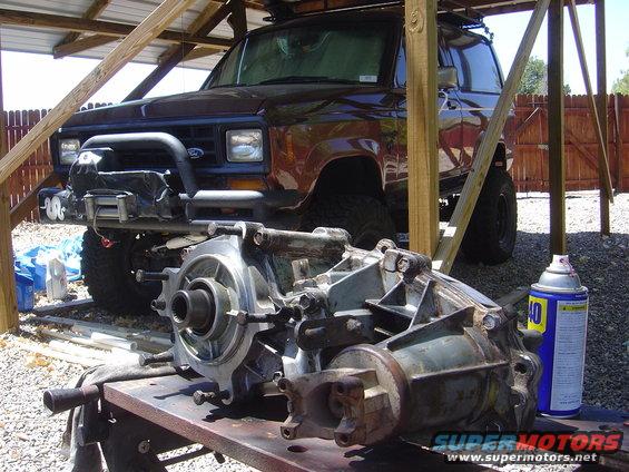 Brown 1986 Ford Bronco II parked under a wooden shelter with transmission parts on a table in front