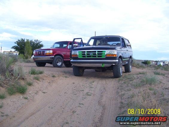 Black 1992 Ford Bronco with green grille and red 1992 Ford Bronco parked on dirt road