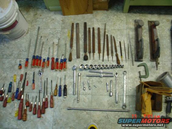 Collection of screwdrivers, wrenches, files, and other tools laid out on a tiled floor