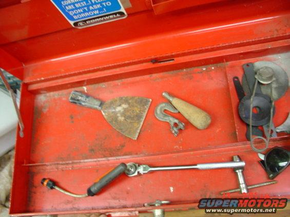Open red toolbox with a rusty putty knife, a hook, a wooden-handled tool, a socket wrench, and other metal parts