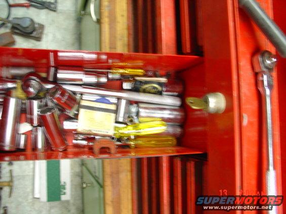 Open red toolbox drawer filled with sockets, wrenches, and screwdrivers. A key is in the lock
