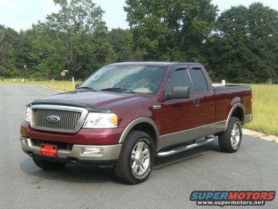 Maroon and tan Ford F-150 pickup truck parked on asphalt, trees and grass in background