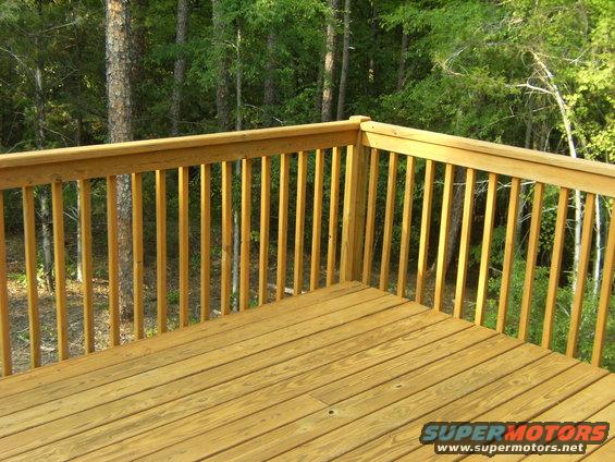 Wooden deck railing and floor with trees in the background. Supermotors logo in the corner