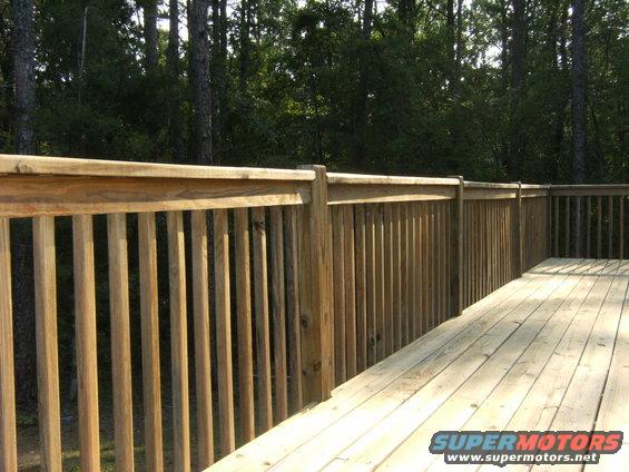 Wooden deck railing and planks with trees in background. Supermotors.net logo in corner