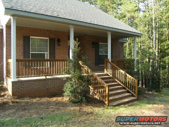 Brick house with wooden porch and stairs, surrounded by trees