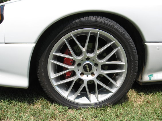 Silver multi-spoke wheel with red brake caliper on a white car