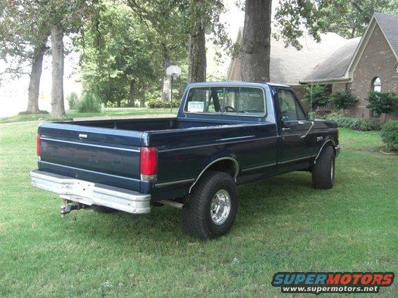 Dark blue pickup truck parked on grass, rear view. Chrome bumper and wheels