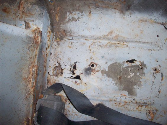 Interior panel of a vehicle showing significant rust and a black seatbelt
