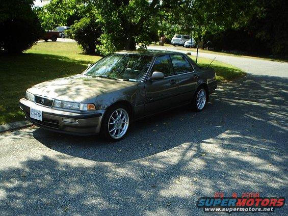 Gray sedan with aftermarket wheels parked on a paved surface under trees