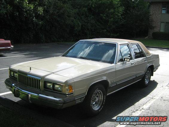 1988 Mercury Grand Marquis sedan parked in a lot, with a red car partially visible to the left