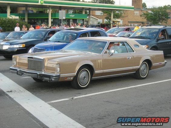 Tan Lincoln Continental Mark V coupe parked in line with other cars at a gas station