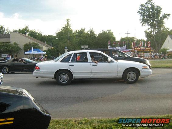 White sedan, side view, driving on a road with a black car behind it