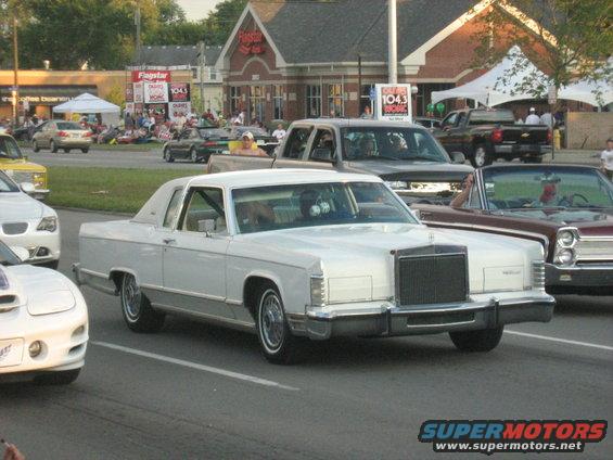 White Lincoln Continental Mark IV driving, other cars and people in background