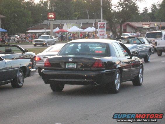 Black sedan from rear, showing taillights, license plate, and chrome wheels