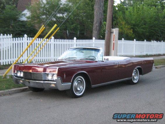 Maroon convertible parked on street, white fence behind it