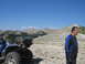 2008 Honda RANCHER - A man stands near a blue ATV on a rocky mountain slope under a clear blue sky.