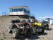 2008 Honda RANCHER - Several ATVs are parked on a gravelly slope near a small building under a clear blue sky.