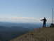 2008 Honda RANCHER - A person stands on a rocky mountain summit, gesturing towards a vast landscape of layered blue mountains under a clear sky.