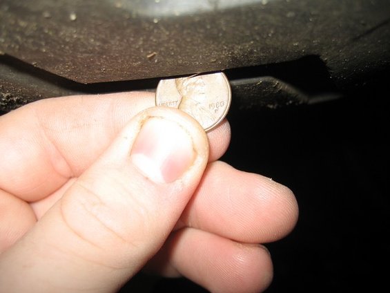 hand holding penny showing 1980 date under dark vehicle part
