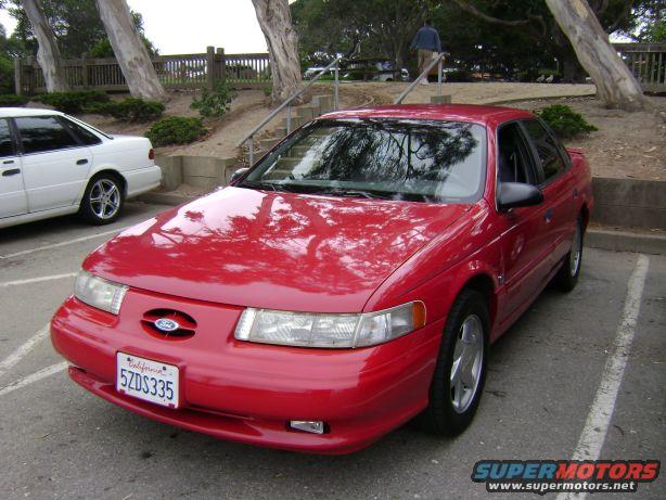 Red 1991 Ford Taurus parked next to a white car. Front end visible with California plates