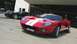 2003 Ford Crown Victoria - A red Ford GT with white racing stripes is parked in front of a hangar, with a black Ford GT behind it.