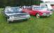 2003 Ford Crown Victoria - Two vintage cars, a black one and a red one, are parked on a grassy field with trees in the background.