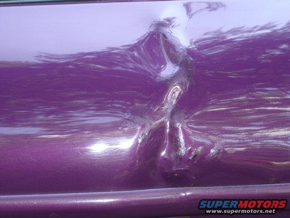 Purple car door with a large dent and scraped paint
