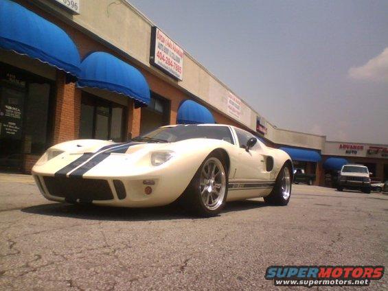 Cream-colored Ford GT40 replica with blue stripes parked in front of a strip mall