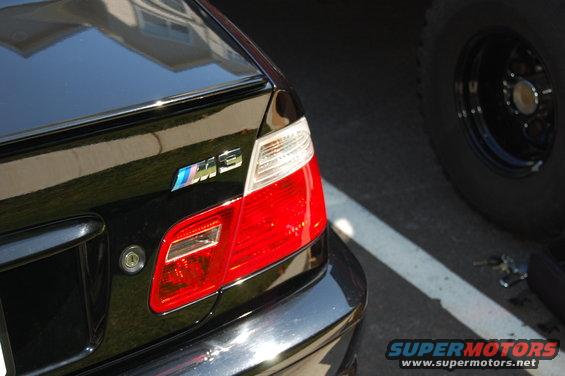 Black BMW M3 with M3 badge and red taillights. Another vehicle's tire is visible to the right