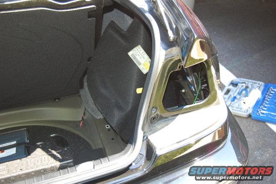 Rear taillight removed, showing trunk interior and wiring. Tools nearby