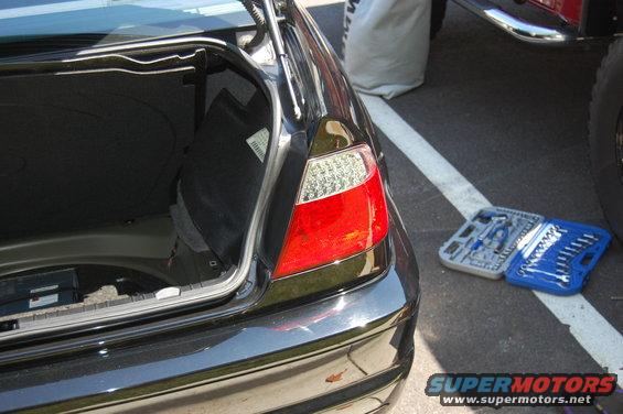 Car trunk open, showing taillight and tools on the ground