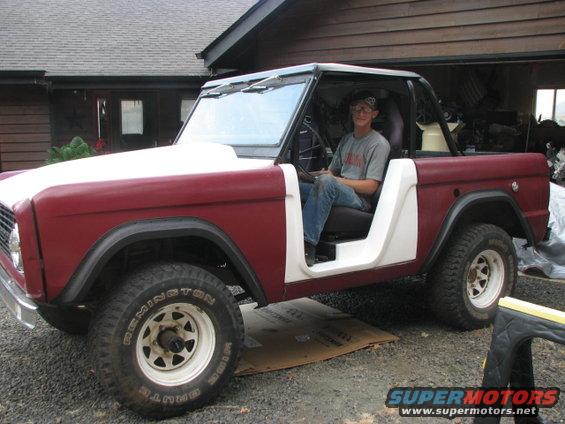 Man sitting in a red and white 1968 Ford Bronco with the doors removed