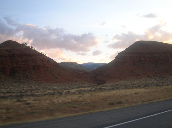 Roadside landscape with red rock formations and a cloudy sky at dusk
