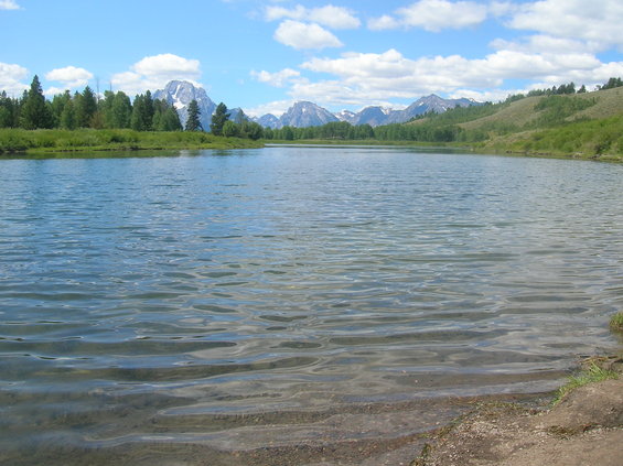 Lake with mountains and trees under a cloudy blue sky