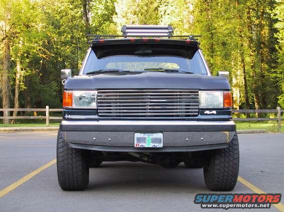 Front view of a dark-colored Ford F-Series truck, possibly from the late 1980s, with a roof-mounted light bar