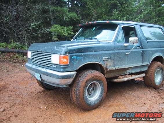 Dark blue Ford Bronco with mud-caked tires on a dirt road
