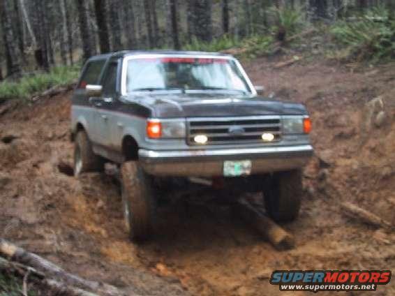 1989 Ford Bronco driving on a muddy, wooded trail