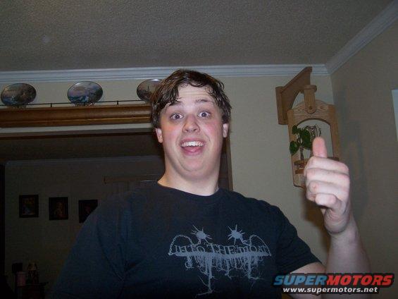 guy with surprised expression gives a thumbs up, wearing a black t-shirt with a band logo