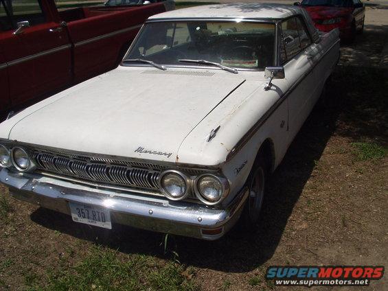 White 1962 Mercury sedan with chrome grille and bumper, parked next to a red truck