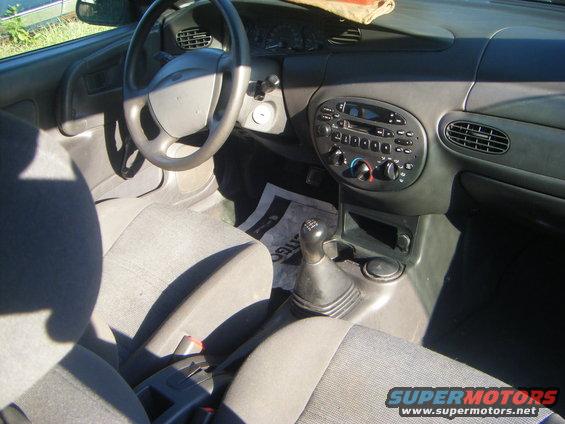 Interior of a car with gray seats, dashboard, steering wheel, and radio. Manual transmission shifter is visible