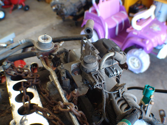 Engine components with metal chains draped over them. A purple toy vehicle is visible in the background