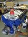 1964 Ford Galaxie - A blue engine block with a red distributor cap and silver pulley is displayed on an orange stand in a workshop.