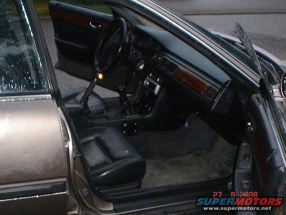 Car interior with open doors, black leather seats, wood trim, and a dashboard with a radio