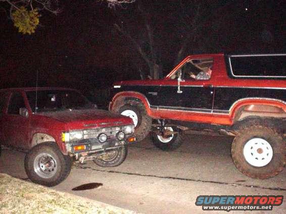 Red and black Ford Bronco lifted with large tires, parked next to a red pickup truck
