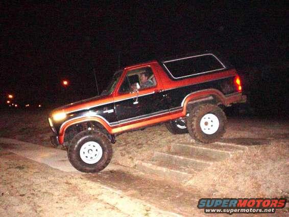 Black and orange 1984 Ford Bronco driving up stairs