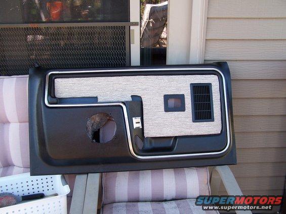 Black and silver door panel with speaker hole and vent, resting on outdoor furniture